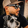Tobby Vasquez is registered to the contest to win money with this photo: man, dog, schnauzer, portrait, sunglasses, cap, beard, facial_hair, black_shirt, pet, companion, outdoor, urban, brick_wall, reflection, closeup, scruffy_fur, collar, side_profile, fashion
