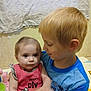baby, child, blond_hair, blue_shirt, pink_clothing, indoor, affection, holding, curious, portrait, siblings, young_boy, infant, casual_clothing, wall, fabric, candid, family, cute, toddler