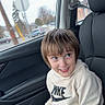 child, boy, car_interior, seat, clothing, hoodie, nike_logo, pants, clipboard, smile, casual, window, daytime, urban, seatbelt, hair, face, person, portrait, happy