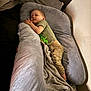 child, toddler, sleeping, bed, blanket, pillow, cushion, clothing, green_shirt, pants, indoor, resting, nap, cute, cozy, person, home, comfort, soft, peaceful
