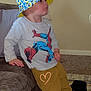 toddler, child, bucket_hat, spiderman_shirt, yellow_pants, blue_sneakers, couch, carpet, indoor, wall, footwear, person, side_view, casual_pose, expression, young_child, clothing, furniture, home, leaning