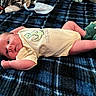 baby, infant, blanket, plaid, blue, onesie, dinosaur, slippers, green, clothing, cute, lying_down, person, newborn, indoor, soft_lighting, face, skin, expression, cozy