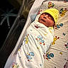 newborn, baby, swaddled, blanket, yellow_hat, sleeping, hospital, bassinet, infant, peaceful, cute, child, person, resting, soft_lighting, duck_pattern, bed, maternity, newborn_care, cozy