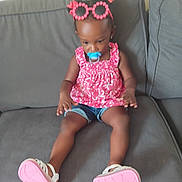 Bella joined the competition — help win amazing prizes! baby, casual, child, cute, denim_shorts, footwear, furniture, glasses, gray_couch, hair_buns, indoor, pacifier, person, pink_bows, pink_clothing, portrait, sitting, toddler, white_sandals, young_child
