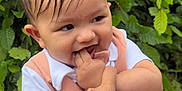 Aadhvin is registered to the contest to win money with this photo: baby, child, person, hand, finger, playing, outdoor, greenery, leaves, nature, cute, infant, clothing, white_shirt, peach_outfit, smile, happy, face, portrait, holding