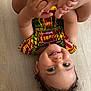 baby, child, colorful_clothing, curly_hair, cute, earrings, face, feet, hands, happy, head, indoor, patterned_outfit, person, playful, skin, smiling, toddler, upside_down, wooden_floor