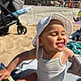 baby, child, beach, sand, sun_hat, tank_top, playing, smiling, sunlight, outdoor, towel, stroller, summer, happy, cute, earrings, tongue_out, sitting, daytime, vacation