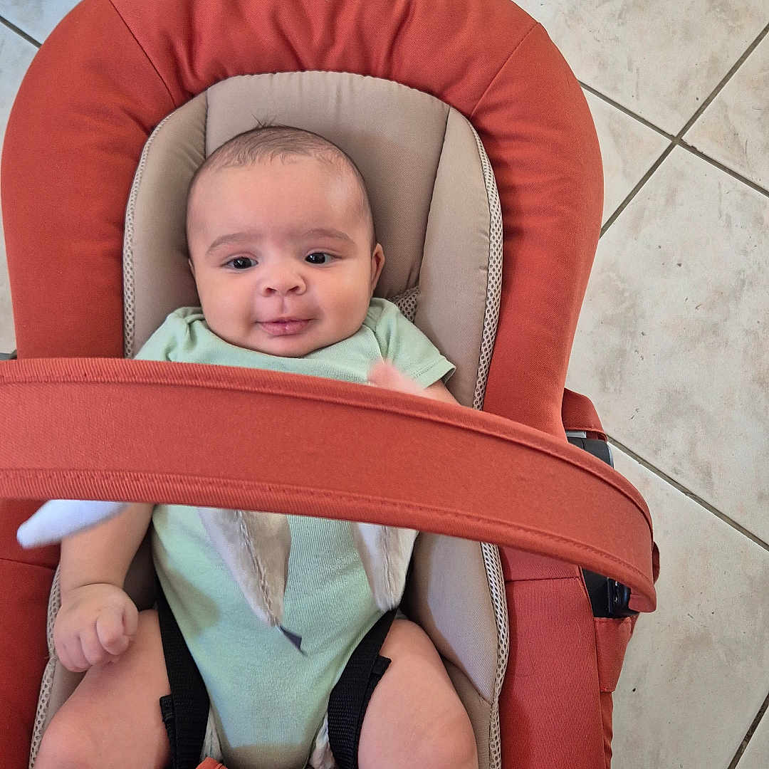 Jaël a rejoint le concours — aidez-le/la à gagner de superbes lots ! baby, baby_carrier, baby_clothing, baby_expression, baby_face, baby_gesture, baby_hands, baby_legs, baby_pose, baby_rocker, baby_safety, baby_seat, baby_smile, child, floor_tiles, indoor, infant, onesie, seatbelt, tiled_floor