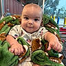 baby, infant, child, blanket, green_blanket, football_pattern, shopping_cart, indoor, clothing, american_flag, cute, chubby_cheeks, portrait, expression, sitting, hand, face, eyes, head, store