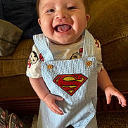 Ezequiel joined the competition — help win amazing prizes! baby, child, smiling, superman, overalls, clothing, indoor, couch, happy, tongue_out, person, carpet, bag, cute, playful, shorts, footwear, bright, portrait, young