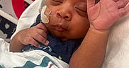 Hezekiah joined the competition — help win amazing prizes! baby, bedding, blanket, close_up, crib, dark_skin, face, feeding_tube, hand, hospital, indoors, infant, medical_tape, newborn, peaceful, portrait, raised_hand, sleeping, striped_blanket, swaddle