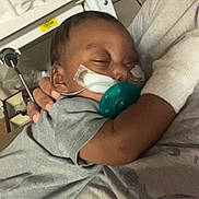 Hezekiah joined the competition — help win amazing prizes! adult, baby, bed, bed_rail, blanket, caregiving, closed_eyes, cuddling, face, gray_clothing, hospital, indoors, infant, medical_tubing, pacifier, parent, photograph, portrait, resting, sleeping