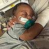 adult, baby, bed, bed_rail, blanket, caregiving, closed_eyes, cuddling, face, gray_clothing, hospital, indoors, infant, medical_tubing, pacifier, parent, photograph, portrait, resting, sleeping