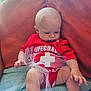 baby, infant, red_clothing, lifeguard_onesie, tulle, blanket, cushion, indoors, cute, chubby_cheeks, sitting, looking_down, soft_light, skin, head, hand, legs, toddler, child, portrait