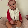 baby, infant, child, headband, vest, red_clothing, socks, wall_stickers, cat_sticker, pink_bow, smiling, sitting, indoor, soft_surface, cute, happy, person, portrait, decor, cozy