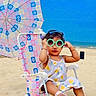 toddler, child, beach, sunglasses, umbrella, chair, sand, dress, footwear, sunny, blue_sky, patterned, colorful, summer, vacation, outdoor, cute, fashion, accessory, relaxation