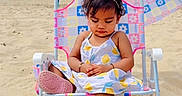 Kridha is registered to the contest to win money with this photo: toddler, child, beach, sand, umbrella, chair, sunglasses, sunny, dress, footwear, blue_sky, outdoor, summer, vacation, cute, relaxing, accessory, patterned, playful, holiday
