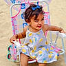 Kridha is registered to the contest to win money with this photo: toddler, child, beach, sand, umbrella, chair, dress, blue_bow, pink_crocs, smile, happy, sunny, outdoor, footwear, sunglasses, colorful, patterned, summer, playful, relaxing