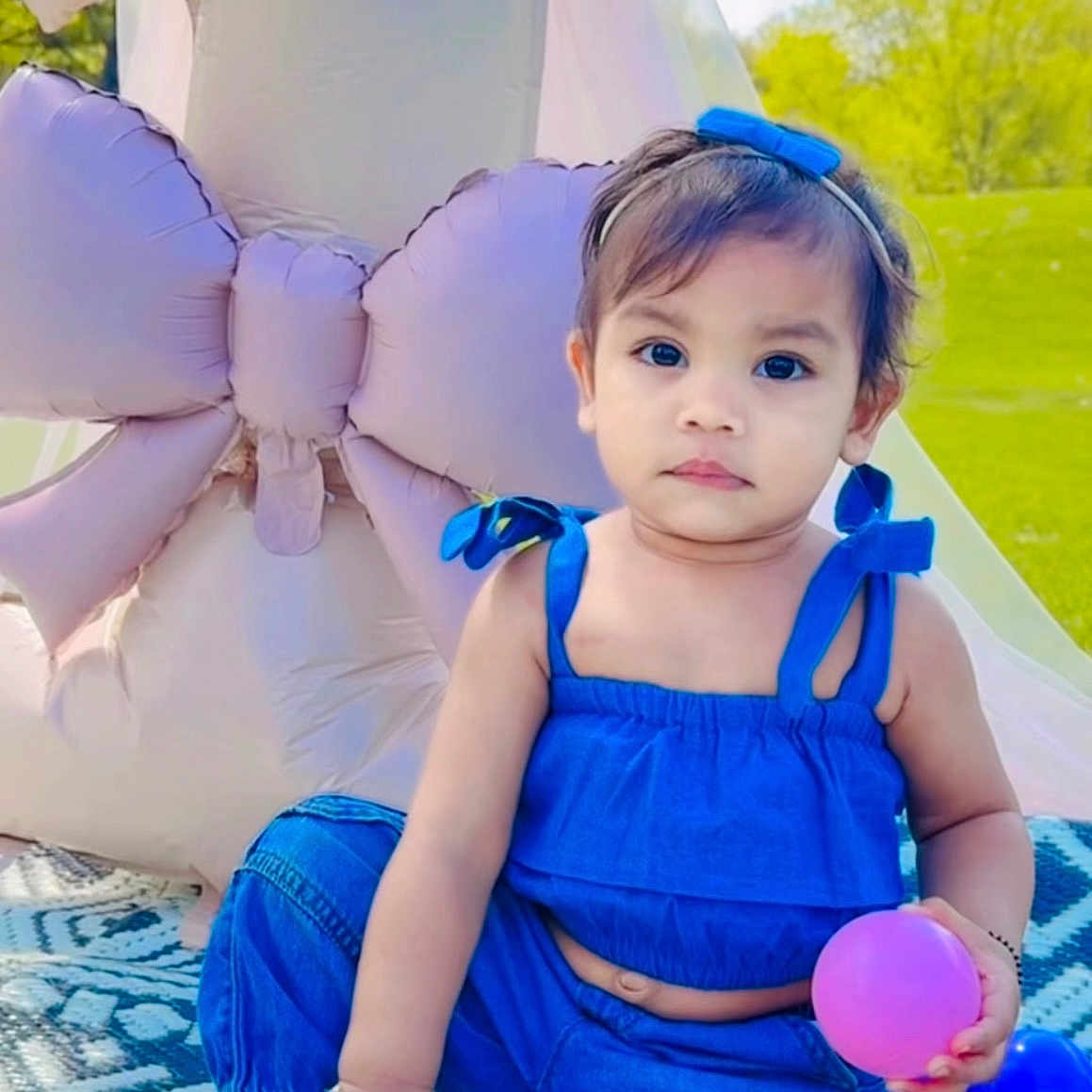 Kridha is registered to the contest to win money with this photo: toddler, child, blue_clothing, ball, inflatable_balloon, outdoor, grass, sky, clouds, patterned_blanket, headband, sneakers, portrait, greenery, sunny, park, cute, baby, kneeling, accessory