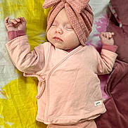 Arianna a rejoint le concours — aidez-le/la à gagner de superbes lots ! baby, sleeping, pink_clothing, headwrap, bow, infant, cozy, cushion, yellow_background, soft_fabric, peaceful, child, portrait, indoor, cute, newborn, relaxed, hands_up, closeup, resting