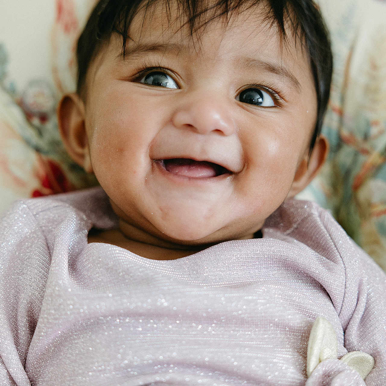 Ishani is registered to the contest to win money with this photo: baby, background, child, closeup, clothing, cute, eyes, face, fashion, happy, head, indoors, infant, mouth, person, portrait, sitting, skin, smiling, young