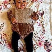 Jannah participe au concours pour gagner de l'argent avec cette photo : baby, smiling, infant, blanket, floral_pattern, clothing, knitted_vest, tights, cute, happy, portrait, child, laying_down, indoors, soft_texture, face, hands, legs, fashion, warm