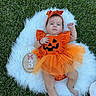baby, infant, child, halloween, pumpkin_costume, orange_dress, bow, grass, outdoor, milestone_photo, three_months, fluffy_blanket, jack_o_lantern, lying_down, portrait, cute, baby_photography, raised_fist, wooden_sign, tulle_skirt