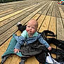 baby, child, dock, wood, outdoor, water, fishing_rod, jacket, clothing, nature, grass, riverbank, person, infant, blue_shirt, sunlight, daylight, face, expression, relaxing