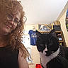 Shadow is registered to the contest to win money with this photo: animal, black_and_white_cat, box, casual, cat, ceiling, clothing, curly_hair, face, fan, glasses, hanger, home, indoor, pet, portrait, shelf, shirt, window, woman