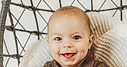 Cory is registered to the contest to win money with this photo: baby, child, smiling, dimple, plaid_overalls, brown_shirt, hanging_chair, woven_chair, blanket, cozy, indoors, portrait, cute, happy, playful, infant, person, seated, bright, soft_light