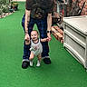 Cory joined the competition — help win amazing prizes! baby, adult, walking, green_turf, plaid_pants, brick_wall, garden, outdoor, smiling, holding_hands, slippers, child, tattoo, person, casual_clothing, first_steps, happy, support, daylight, patio