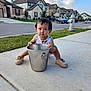 toddler, child, bucket, sidewalk, shoes, grass, suburban, houses, car, fire_hydrant, sky, clouds, curious, outdoor, daylight, concrete, casual, expression, street, residential_area