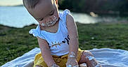 Wrenley is registered to the contest to win money with this photo: baby, blanket, cake, celebration, child, cute, frosting, fun, grass, messy, nature, outdoor, playful, portrait, sitting, summer, sunset, water, white_shirt, yellow_shorts