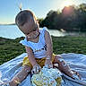 baby, blanket, cake, celebration, child, cute, frosting, fun, grass, messy, nature, outdoor, playful, portrait, sitting, summer, sunset, water, white_shirt, yellow_shorts