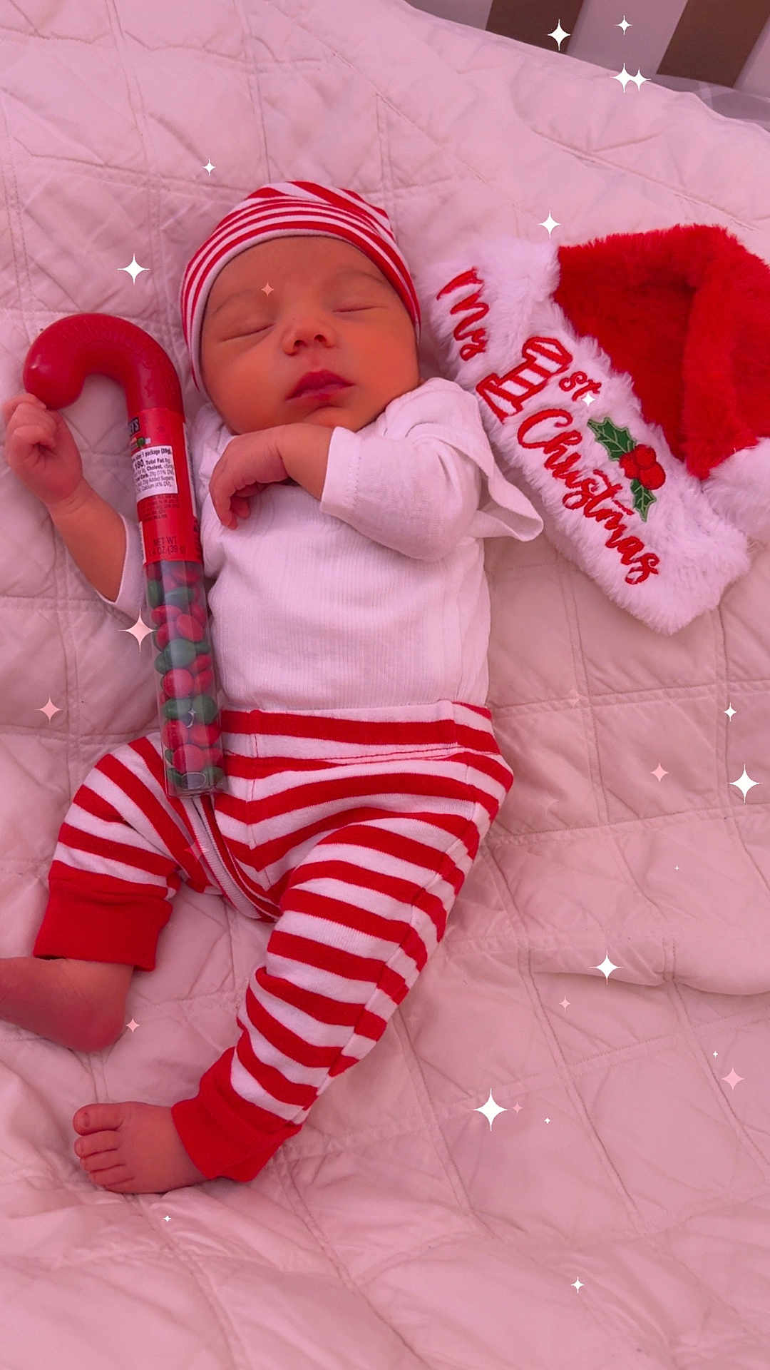 Iñaki is registered to the contest to win money with this photo: baby, sleeping, christmas, holiday, festive, red_and_white, striped_clothing, hat, candy_cane, candy, quilted_blanket, santa_hat, infant, cute, peaceful, bed, pajamas, celebration, cozy, sparkles