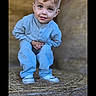 child, boy, pajamas, hay, bale, barn, rural, outdoor, curious, crouching, blue_clothing, smiling, portrait, young_child, cute, innocent, casual, daylight, nature, farm