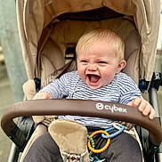 Finley is registered to the contest to win money with this photo: baby, stroller, laughing, child, toy_rings, pacifier, striped_shirt, beige, outdoor, happy, infant, clothing, seatbelt, grip, person, cute, expression, young_child, casual, transport