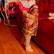 Lamiyah joined the competition — help win amazing prizes! toddler, child, indoor, wooden_floor, red_couch, gold_vest, pink_headband, boots, walking, curious_expression, living_room, furniture, toy, person, clothing, home, floor, face, young_child, cute