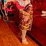 toddler, child, indoor, wooden_floor, red_couch, gold_vest, pink_headband, boots, walking, curious_expression, living_room, furniture, toy, person, clothing, home, floor, face, young_child, cute