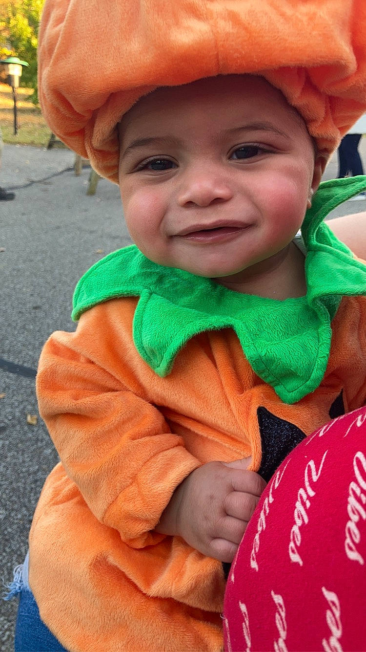 Jaylani is registered to the contest to win money with this photo: baby, cap, chin, eye, face, facial_expression, finger, happy, head, headgear, headwear, iris, joy, lip, mouth, nose, orange, organ, outerwear, person