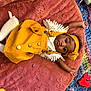 baby, blanket, child, colorful, comfortable, curious_expression, cute, headband, indoor, infant, knitted_blanket, lying_down, person, pink_blanket, playful, red_toy, soft_texture, toy, white_socks, yellow_dress