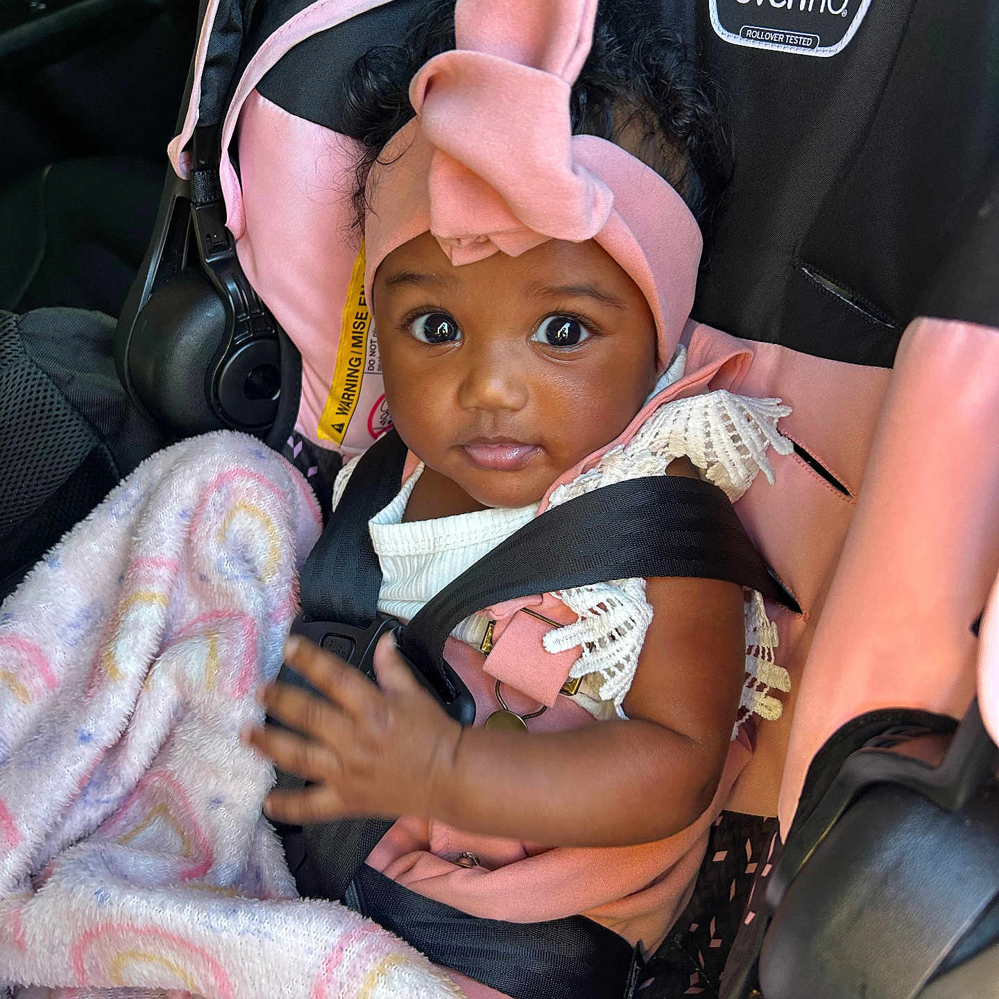 Gabriella is registered to the contest to win money with this photo: baby, baby_girl, blanket, car_interior, car_seat, child, comfortable, curly_hair, cute, headband, indoors, infant, looking_at_camera, person, pink_clothing, portrait, seatbelt, sitting, soft_texture, young_child