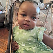 Kay'Lani is registered to the contest to win money with this photo: toddler, child, stroller, green_dress, white_bows, indoor, curious, baby, person, face, hair_bows, seated, cute, infant, fabric, mesh, hand, wooden_floor, background, soft_lighting