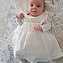 baby, infant, white_dress, lying_down, bedspread, floral_pattern, cute, hands, wide_eyes, soft_lighting, striped_socks, fabric_texture, portrait, indoors, child, young, person, smiling, sleepwear, resting