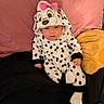 baby, infant, onesie, dalmatian_pattern, pink_bow, hood, pillow, bed, blanket, black_and_white, spots, cute, sleepy, clothing, child, indoor, soft_toys, yellow_pillow, pink_pillow, socks