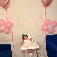 Keilany joined the competition — help win amazing prizes! baby, high_chair, balloon, pink, heart_balloon, flower_balloon, banner, celebration, birthday, smiling, child, indoor, headband, dress, wooden_floor, blue_chair, wall, happy, person, toddler