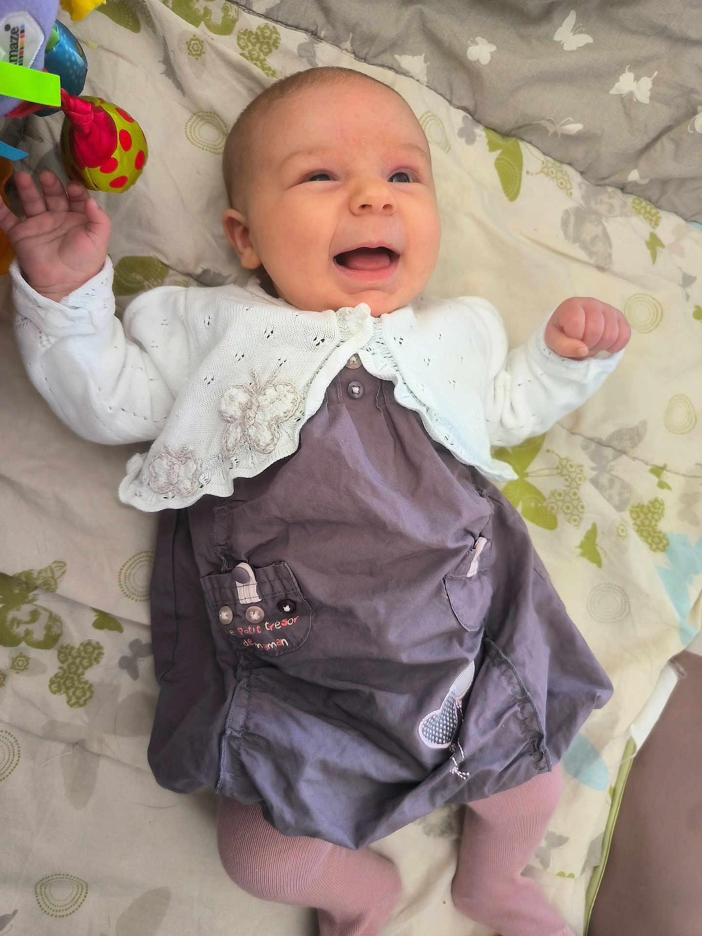 Lina participe au concours pour gagner de l'argent avec cette photo : baby, smiling, infant, blanket, cardigan, dress, toy, pattern, toddler, cute, happy, lying_down, clothing, face, hand, footwear, purple, white, pink, indoor