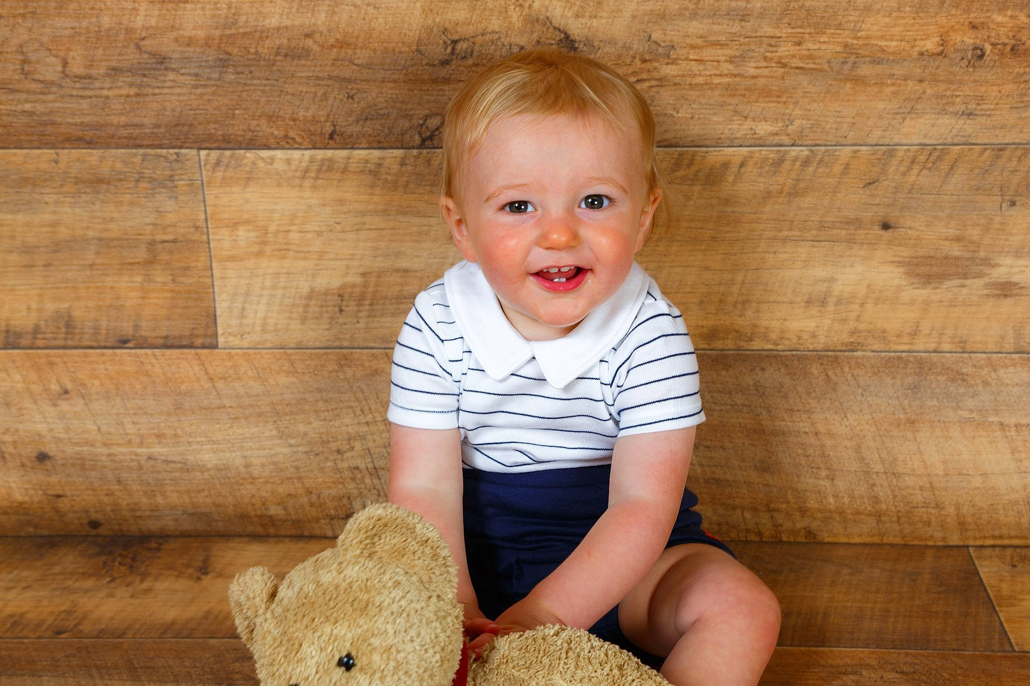 Bobbie is registered to the contest to win money with this photo: baby, baby_toddler_clothing, cheek, child, facial_expression, floor, flooring, fun, happy, hardwood, joy, nose, person, skin, sleeve, smile, standing, stuffed_toy, teddy_bear, toddler