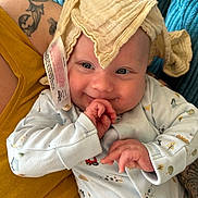 Ludo is registered to the contest to win money with this photo: baby, infant, smile, face, clothing, onesie, hand, adult, arm, tattoo, fabric, blanket, couch, comfort, cute, child, playful, happy, indoor, person