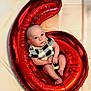 baby, infant, balloon, red_balloon, number_six, checkered_clothing, cute, portrait, smiling, curious, soft_background, indoor, child, newborn, sitting, celebration, festive, hands, feet, head